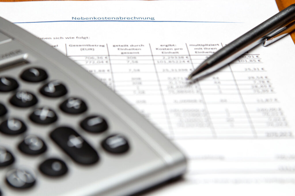 Foto von einem Taschenrechner und einem Stift auf einer deutschen Nebenkostenabrechnung mit unscharfen Zahlen und Spalten.
